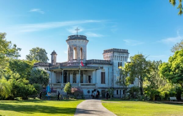 Historic mansion set in lush greenery in Paraguay, showcasing architectural elegance with a tower and cross, under a clear blue sky