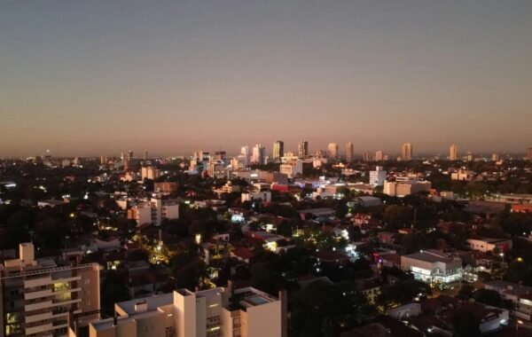 Aerial view of Asunción, Paraguay at dusk, showcasing the city skyline with illuminated buildings and residential areas against a soft twilight sky