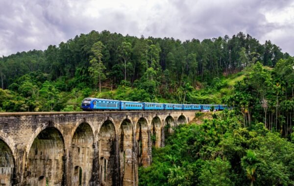 A scenic train traveling across an iconic viaduct in Sri Lanka, surrounded by lush green hills and cloudy skies, showcasing the beauty of the island's landscape