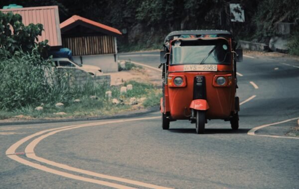 Colorful tuk-tuk driving along a winding road in Sri Lanka, surrounded by lush greenery and local buildings