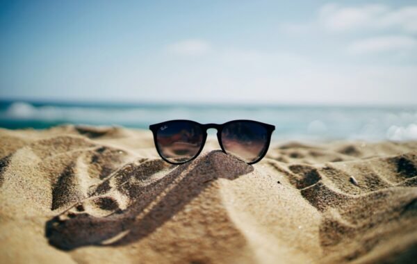 Sunglasses resting on a sandy beach with ocean waves in the background, capturing the essence of summer relaxation and sun-soaked adventures