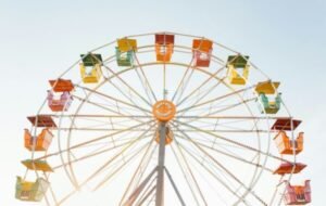 Colorful ferris wheel against a clear sky, showcasing vibrant seats in shades of orange, green, and yellow, evoking a joyful summer atmosphere