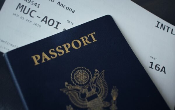 A close-up of a blue passport with the word PASSPORT prominently displayed, resting on a flight ticket showing details for a journey to Ancona from Munich
