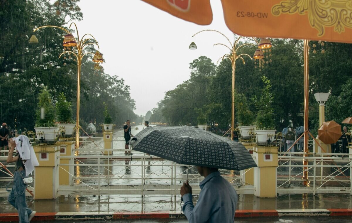 Rainy scene in Vietnam showcasing people with umbrellas amidst lush greenery and decorative light fixtures, reflecting a tranquil ambiance