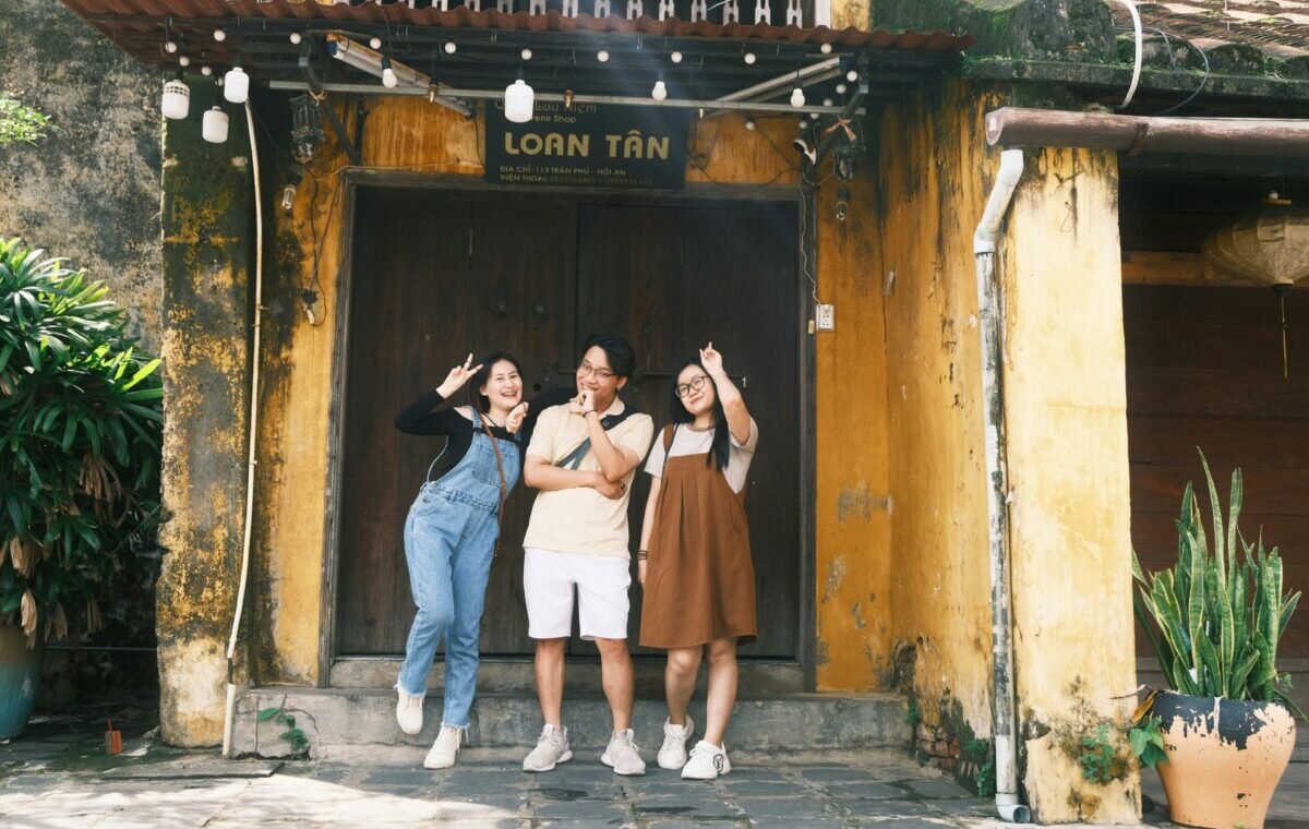Three friends posing playfully in front of a charming yellow building, enjoying their travels together