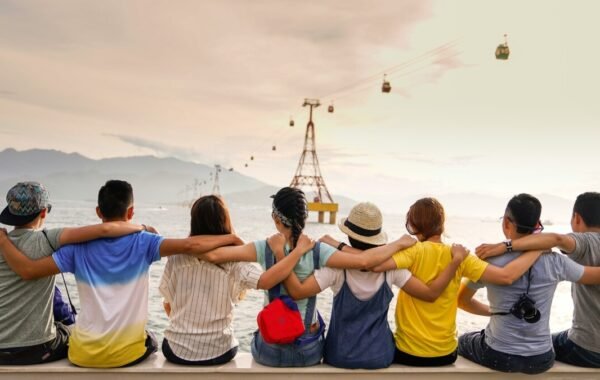 A group of friends enjoying a picturesque travel moment, sitting together with their arms around each other, overlooking a serene landscape and cable cars in the distance