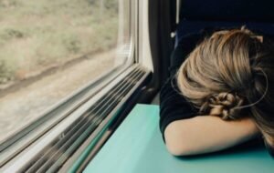 A weary traveler resting her head on a table in a train, illustrating the exhaustion often associated with jet lag