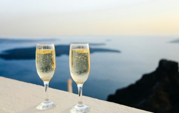 Two elegant champagne flutes filled with bubbly drink, set against a stunning sunset view of the sea and cliffs, capturing a luxurious moment