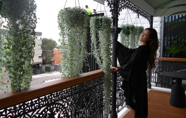 Woman in a black dress enjoying a luxurious balcony adorned with hanging greenery and intricate wrought iron details, capturing a serene and elegant atmosphere