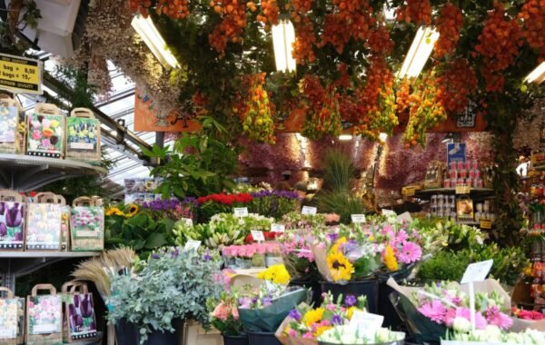 Vibrant flower market in Amsterdam showcasing an array of colorful blooms, including tulips and sunflowers, surrounded by hanging orange decorations and lush greenery