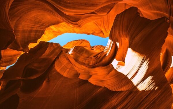 Vibrant orange sandstone walls of Antelope Canyon framed by a blue sky, showcasing the canyon's unique rock formations and natural light