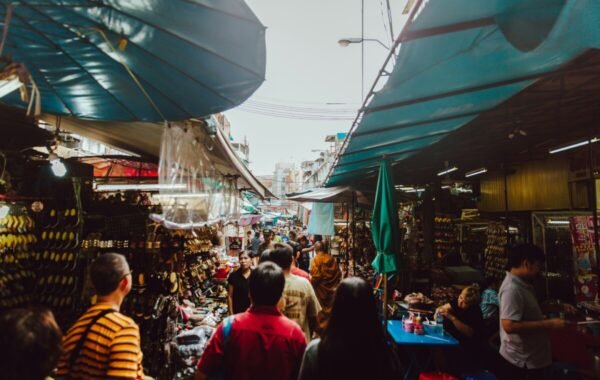 Bustling market scene in Bangkok, showcasing vibrant stalls filled with goods and shoppers exploring the lively atmosphere under blue awnings