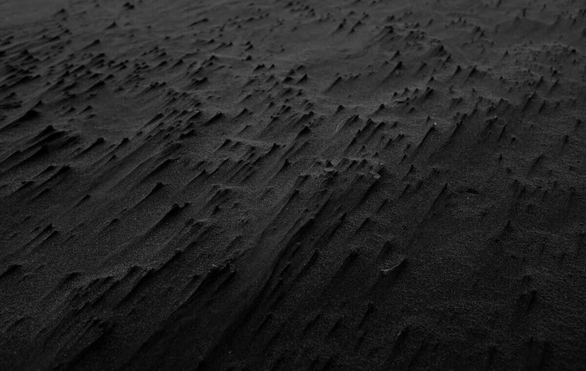 Close-up view of a black sand beach, showcasing intricate patterns and textures in the dark volcanic sand