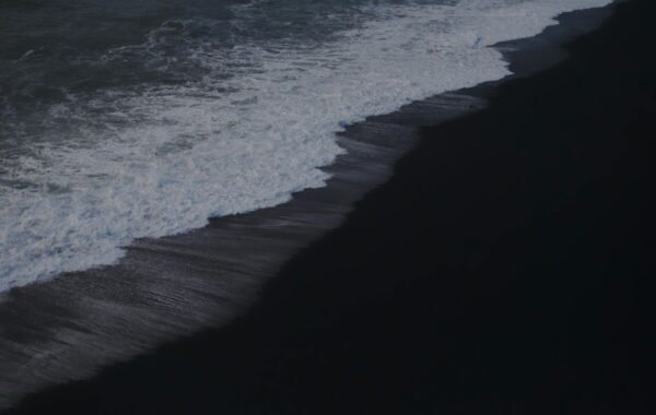 Waves crashing on a black sand beach, showcasing a dramatic contrast between the dark shoreline and frothy white surf