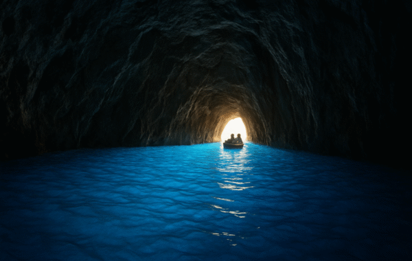 A small boat navigates through the serene, illuminated waters of the Blue Grotto in Italy, surrounded by rocky cave walls and vibrant blue water reflecting the light at the entrance