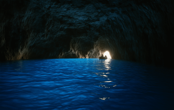 A tranquil view of the famous Blue Grotto in Italy, featuring a serene blue sea illuminated by light from an opening in the cave, with a small boat navigating the calm waters
