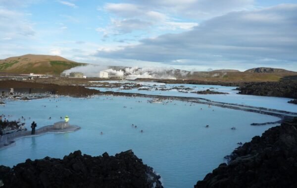 Stunning view of the Blue Lagoon in Iceland, featuring luminous turquoise waters surrounded by rugged lava landscapes, with steam rising in the background and visitors enjoying the thermal pool