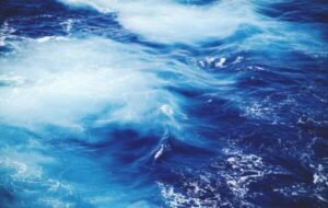 Vibrant blue ocean waves with swirling patterns and foamy white highlights, showcasing the beauty of marine waters