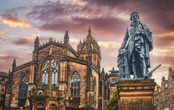 Statue of Adam Smith in front of a historic building in Edinburgh, Scotland, under a dramatic sunset sky