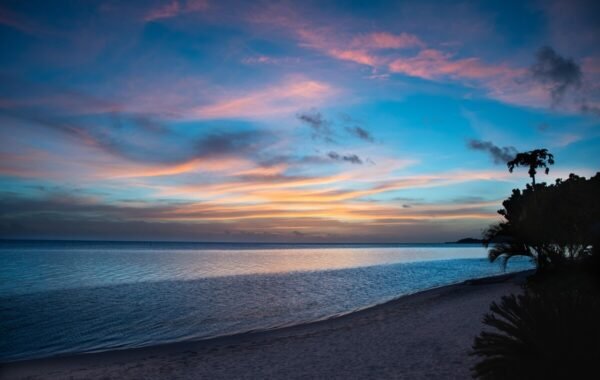 Serene beach sunset over calm waters, showcasing vibrant hues of orange, pink, and blue