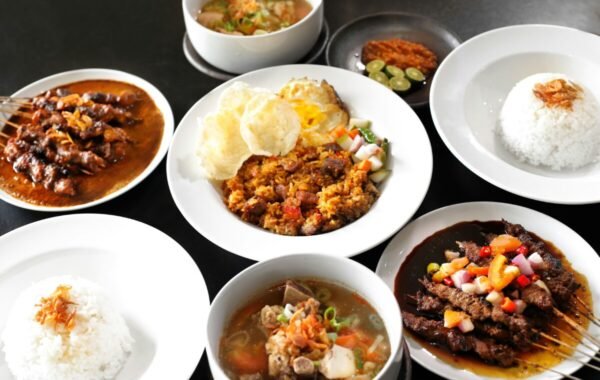 A vibrant spread of traditional Indonesian dishes, featuring grilled satay, savory rice, and various soups alongside fried rice garnished with crispy onions and fresh vegetables