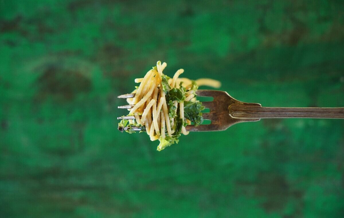 A fork holding a serving of pasta mixed with fresh greens, set against a vibrant green background, highlighting a delicious Italian food dish