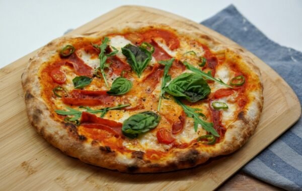 Delicious Italian pizza topped with fresh basil, spicy chilies, and vibrant tomatoes, presented on a wooden cutting board