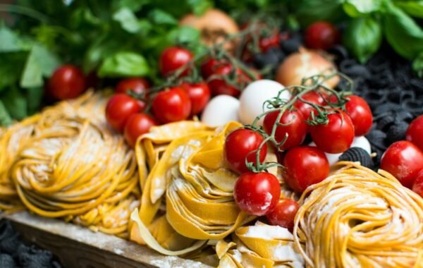 Fresh Italian ingredients featuring vibrant red cherry tomatoes, artisanal pasta, and green basil leaves, beautifully arranged with eggs, creating an inviting culinary display