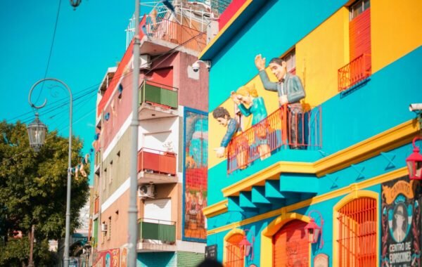 Vibrant street scene in La Boca, Buenos Aires, showcasing colorful buildings adorned with artistic murals and figures on balconies, set against a clear blue sky