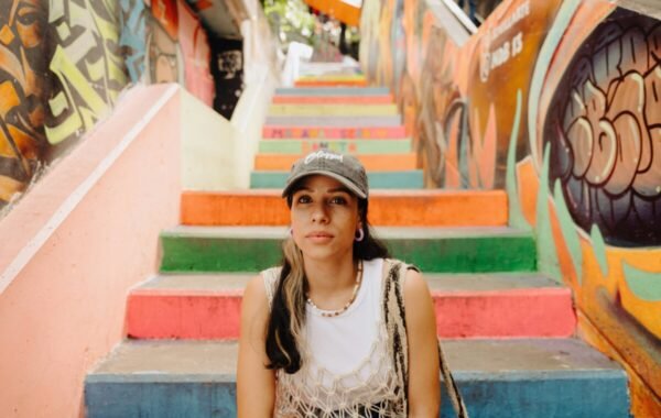 A young woman sits on vibrant, multicolored stairs in Medellín, Colombia, surrounded by colorful street art and murals