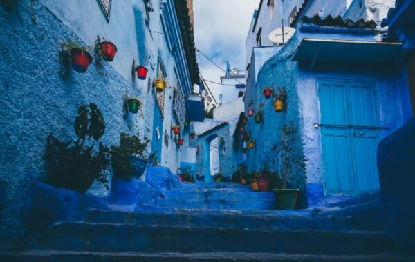 Charming blue alleyway in Morocco adorned with colorful flower pots and lanterns, capturing the vibrant essence of local architecture