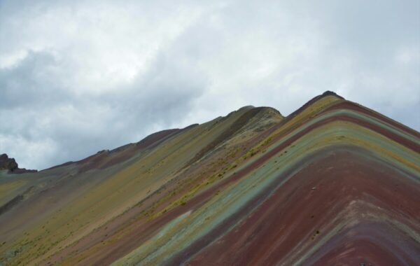 Stunning view of the Rainbow Mountains in Peru, showcasing vibrant, multi-colored layers of rock under a cloudy sky