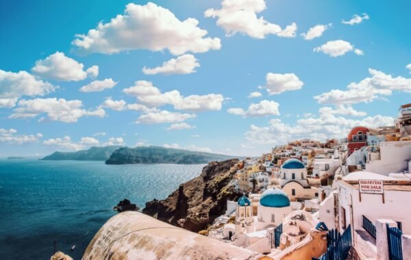 Breathtaking view of Santorini's iconic white-washed buildings and blue-domed churches overlooking the Aegean Sea, with stunning clouds in a vibrant sky