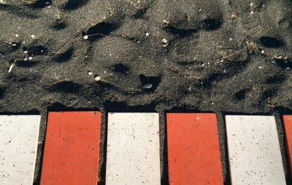Close-up view of intersecting red and white stones on the ground next to textured black sand, highlighting the unique geological features of Santorini's landscape