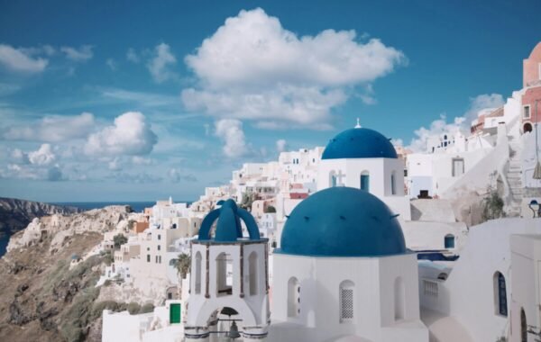 A stunning view of Santorini’s iconic white buildings with blue domes against a bright sky, showcasing the island's unique architecture and dramatic cliffside landscape