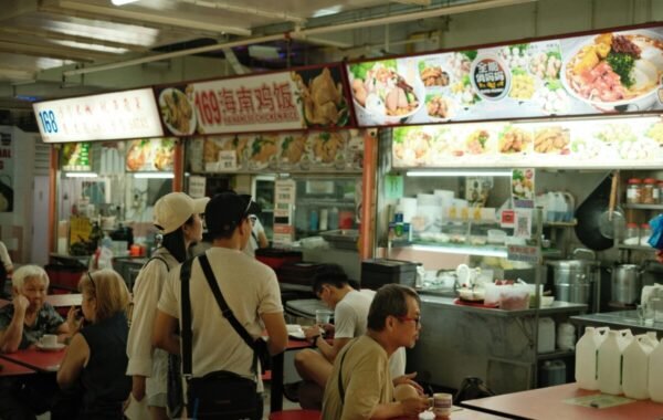 Crowd enjoying diverse Singaporean food at a vibrant hawker center, featuring various food stalls with colorful menus