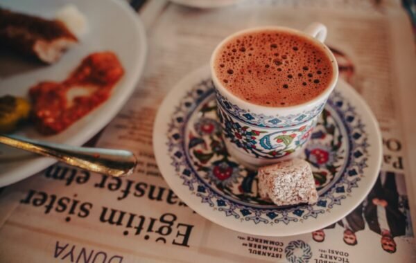 A beautifully decorated cup of Turkish coffee served with a piece of lokum on a patterned plate, resting on a newspaper background
