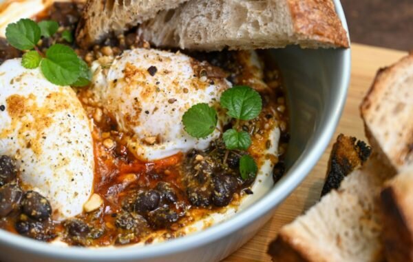 Delicious Turkish dish featuring poached eggs in a spiced sauce, garnished with fresh herbs and accompanied by slices of crusty bread