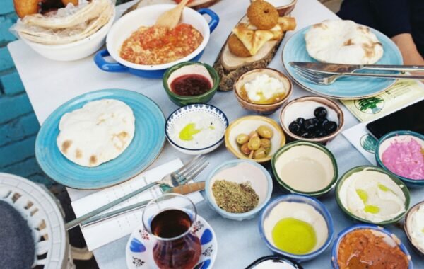 A vibrant spread of traditional Turkish food featuring plates of fresh bread, spicy tomato stew, various dips, olives, pickled vegetables, and a glass of tea on a colorful table setting