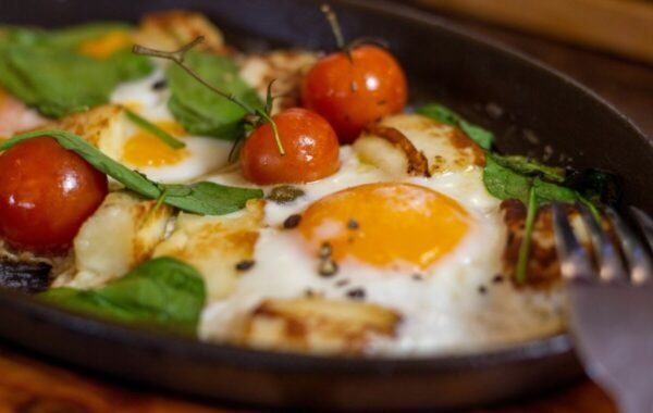 Savory Turkish breakfast dish featuring poached eggs, sautéed cherry tomatoes, and fresh spinach, served in a skillet with grilled cheese