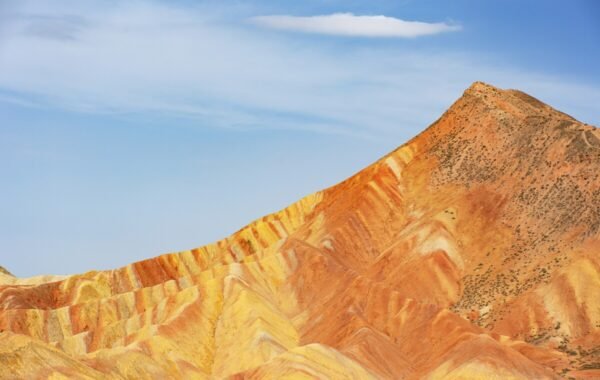 Vibrant, multicolored rock formations of Zhangye Danxia in China, showcasing striking layers of red, orange, and yellow against a clear blue sky