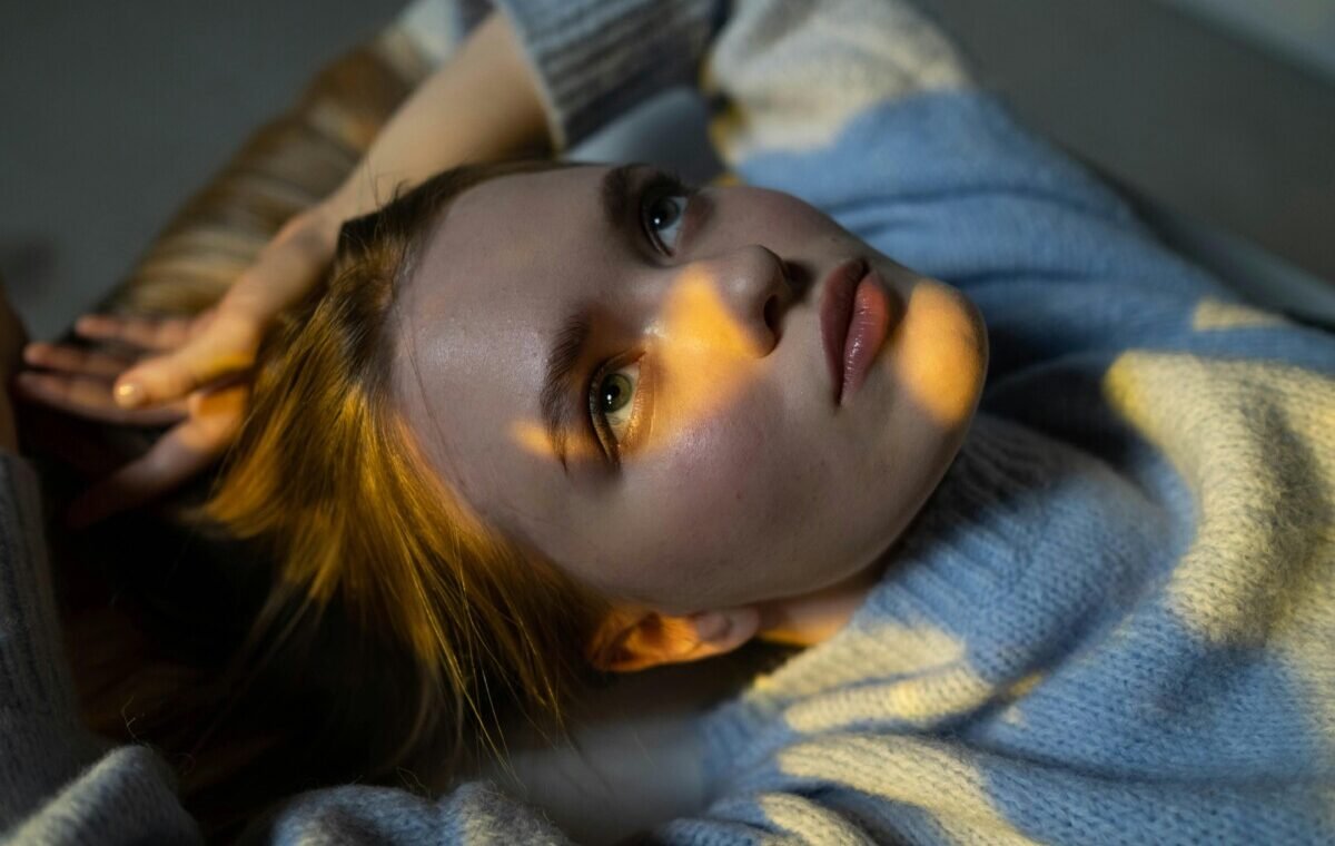 Close-up of a girl with striking features lying down, gazing upward, illuminated by soft natural light
