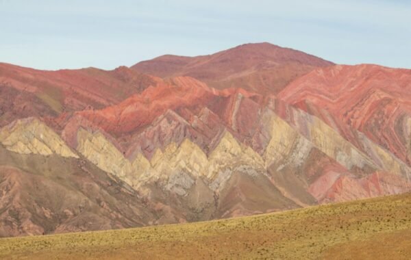 Stunning view of the vibrant, multicolored mountains of Peru, showcasing striking red, yellow, and brown hues in distinct patterns against a clear sky