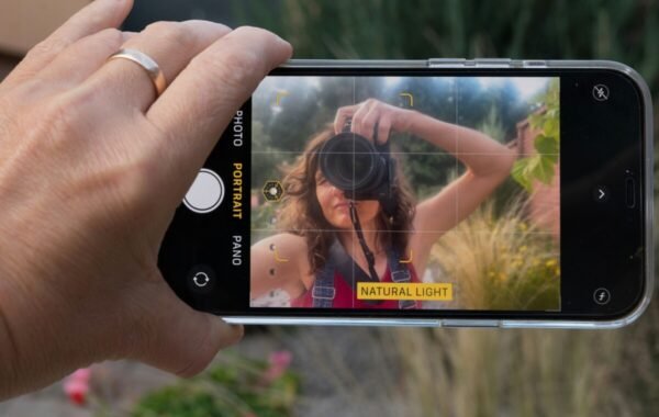 A hand holding a smartphone captures a photographer taking a self-portrait in natural light, showcasing creative photography techniques