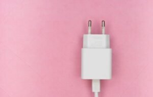White charging plug with two prongs on a pink background, highlighting its minimalist design and practical use for electronic devices