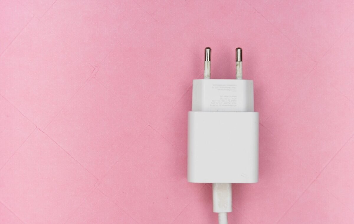 White electrical plug with two prongs, connected to a cable, against a soft pink background