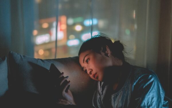 A solo female traveler relaxing indoors, engrossed in her phone, with a soft glow from city lights in the background, capturing the essence of urban exploration and solitude