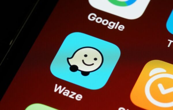 Waze navigation app icon displayed on a smartphone, featuring a smiling cartoon car design on a blue background, surrounded by other app icons