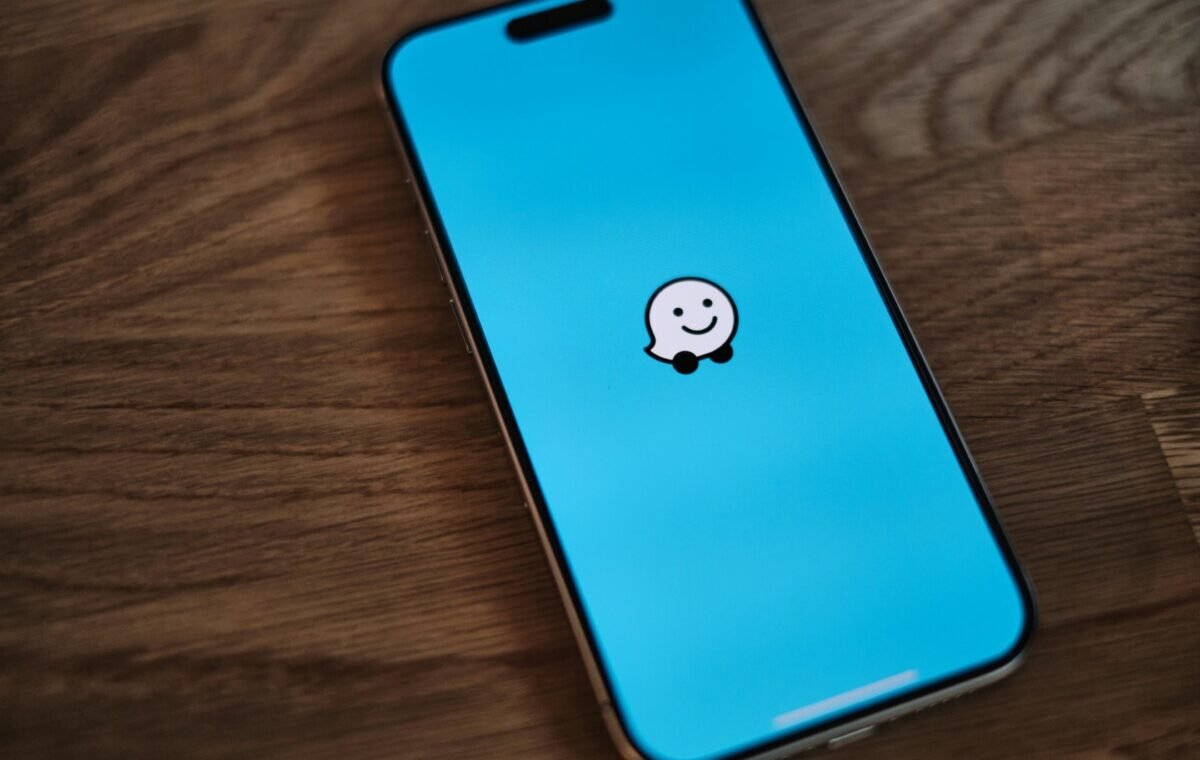 Smartphone displaying the Waze navigation app logo on a bright blue background, positioned on a wooden surface