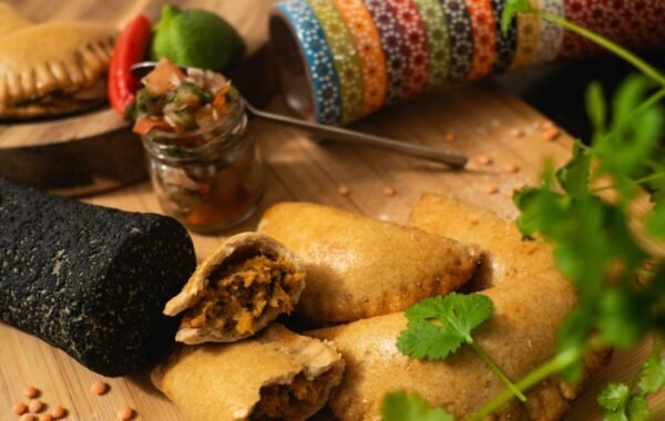 Golden-brown empanadas are displayed alongside fresh ingredients, including cilantro, lime, and chili